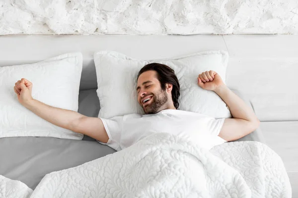 一个人躺在舒适的床上 舒舒服服地躺在家里 开心地微笑着 早上醒来 享受新的一天 复制空间 — 图库照片