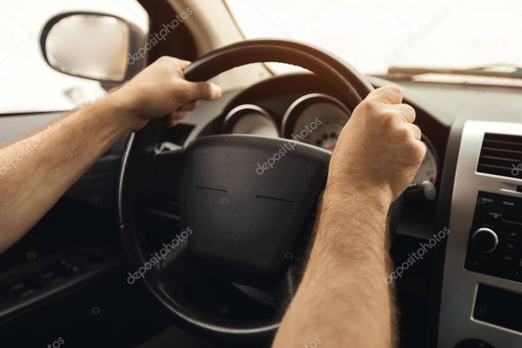 Unrecognizable male driver sitting in a car on drivers seat. Middle aged guy riding in the city, holding hands on steering wheel, back rear over the shoulder view, selective focus