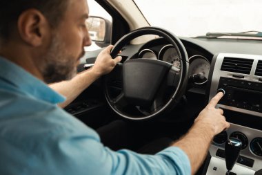 Olgun bir adamın radyo istasyonunu kapatması, arabada müzik dinlemesi, otomobil ses sisteminin tadını çıkarması, yeni aracının düğme açma sesini denemesi, omuz manzarası, seçici odaklanma...