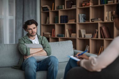 Mutsuz milenyum Avrupalı erkek modern klinikte siyahi kadın psikoloğu dinliyor. Psikolojik problemler, depresyon terapisi ve zihinsel tedavi ve hastanın profesyonel tıbbi desteği