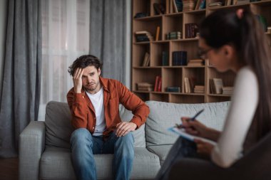 Genç Avrupalı kadın psikolog, modern kliniğin iç kısımlarındaki mutsuz beyaz adama danışıyor. Depresyon, psikolojik sorunlar, terapi ve zihinsel tedavi, profesyonel tıbbi destek ve yardım