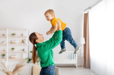 Mutlu anne oğluyla eğleniyor, gülümseyen sevimli bir çocuk büyütüyor, çocuğu kucağında tutuyor, uçuyormuş gibi yapıyor, oturma odasında birlikte oynuyor, mekanı kopyalıyor.