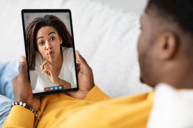 Telekomünikasyon konsepti için mobil uygulama. Milenyum Afrikalı Amerikalı adam modern dijital tablet kullanıyor, evdeki kanepede takılıyor ve güzel kız arkadaşını ya da karısını omzundan vuruyor.