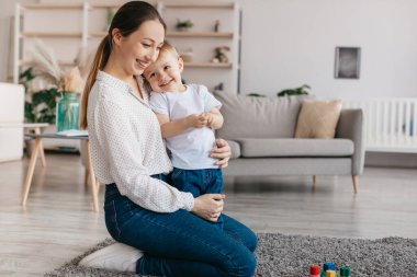 Mutlu annelik kavramı. Genç, sevgi dolu bir anne ve küçük oğlu kucaklaşıyorlar, evde birlikte vakit geçiriyorlar, boş bir alan. Heyecanlı anne çocuğu kucaklıyor ve gülümsüyor.