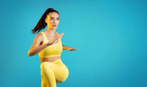 Fit Young Lady Exercising Doing Elbow To Knee Crunch Standing During Cardio Workout Over Blue Studio Background. Sporty Lifestyle And Fitness Motivation Concept. Empty Space For Text