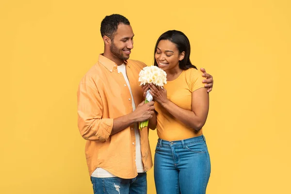 有爱心的年轻黑人男人用黄色的工作室背景把一束水仙花送给他的女朋友 爱戴着一束鲜花的非洲裔美国人夫妇一起庆祝生日 — 图库照片