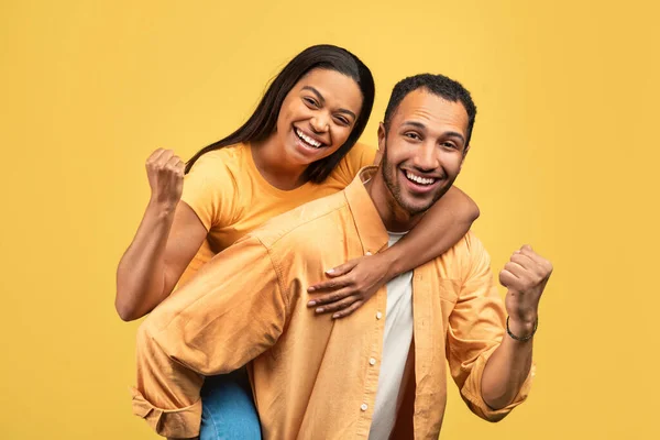 迷人的年轻的非洲裔美国男人让他的女朋友搭便车 在黄色的工作室背景上给他打手势 千年期黑人夫妇快乐 庆祝成功或成就 — 图库照片