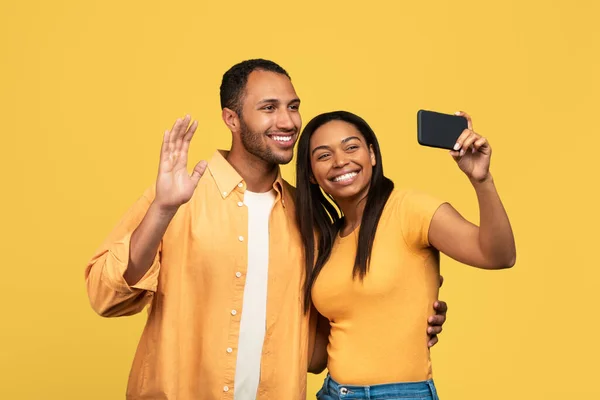 幸せな若い黒のカップルは 黄色のスタジオの背景に自撮りを取り スマートフォンでオンラインでチャットやウェブカメラで手を振って リモートコミュニケーション バーチャルミーティングの概念 — ストック写真