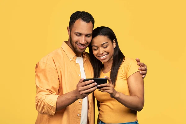 밀레니엄 커플은 휴대폰을 사용하고 문자를 보내고 노란색 스튜디오 배경으로 인터넷을 — 스톡 사진