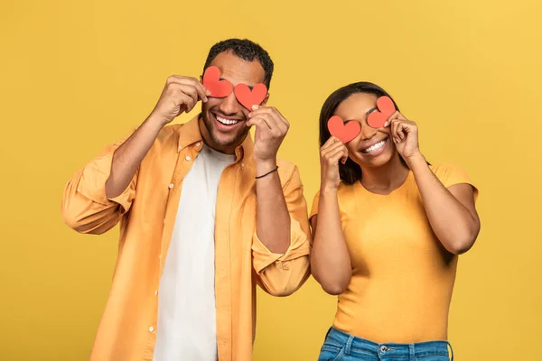 被爱情的概念蒙蔽了双眼深情的非洲裔美国夫妇在黄色的工作室背景上用红纸红心蒙住眼睛 浪漫的黑人男女表达爱意 — 图库照片