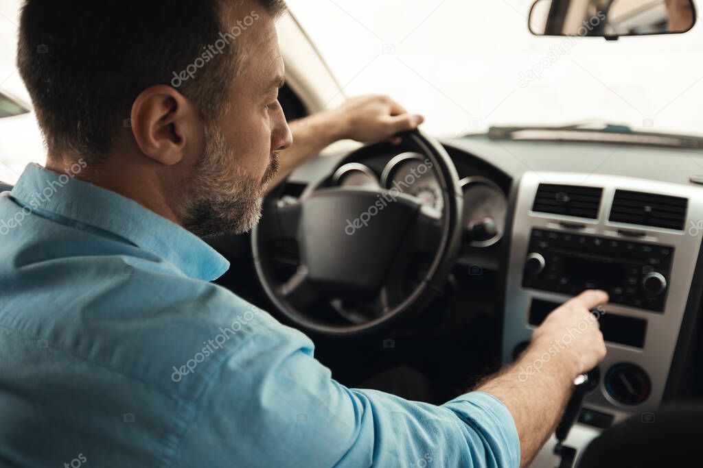 Road Playlist. Rear Back Over Shoulder View Of Man Driving Car And Listening To Music On Auto Audio System, Checking Automobile Options During Test Drive Pushing Button On Dashboard Turning On Radio