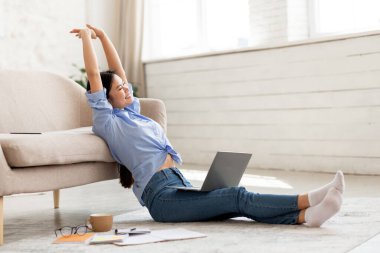 Keyifli genç Çinli kadın oturma odasında yerde oturuyor, dizüstü bilgisayar kullanırken pencereden bakıyor, evden, yandan bakıyor, boşluğu kopyalıyor.