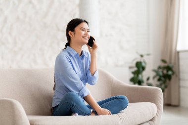 Kanepede oturan, cep telefonuyla konuşan, fotokopi odasına bakan, gülümseyen, rahat, beyaz oturma odası, panorama. İletişim konsepti