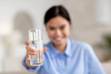 Gülümseyen Asyalı bir kadının elinde bir bardak taze kaynak suyu, bulanık bir arka plan, kopyalama alanı. Milenyum için sağlıklı yaşam biçimi, su içme, su tüketimi kavramları