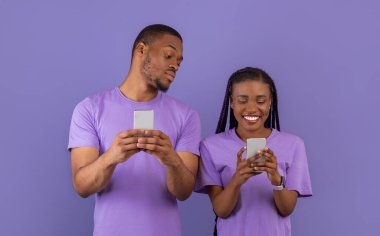 Meraklı siyahi adamın, kız arkadaşlarına akıllı telefonuyla bakmaya çalışan, elinde aletini tutan ve sohbet eden gülümseyen kadının portresi mor menekşe arka planda tek başına duran bir çift. Güvensizlik Konsepti