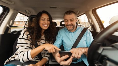 Kısa yol güzergahı. Lüks arabanın içinde oturmuş, akıllı telefonu işaret eden gülümseyen bir çiftin portresi, neşeli erkek sürücü hücresi, yeri gösteriyor, dijital harita uygulaması kullanıyor.
