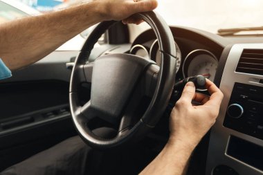 Sürücü koltuğunda arabada oturan ve silecekleri çalıştıran tanınmayan bir adamın omuz manzarasına yakın çekim. Erkek sürücü yağmurda şehirde at sürüyor, direksiyonda el ele tutuşuyor.