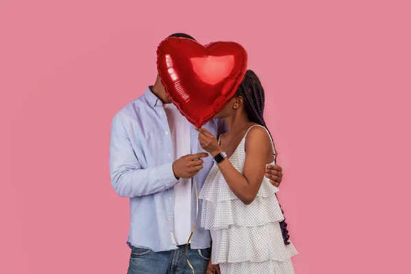 圣瓦伦丁日概念 那对害羞的非洲裔美国夫妇恋爱了 他们抱着红心气球 躲在气球后面 掩面遮掩自己的隐私 与粉红工作室的背景墙隔离 — 图库照片