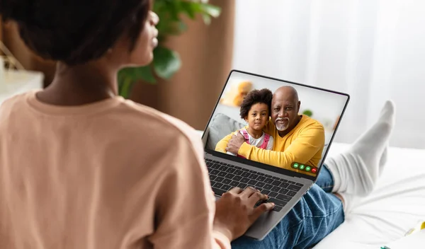 Back view of young black woman calling her family, using computer, african american lady having video conference with senior dad and baby child while staying apart, panorama. Online communication