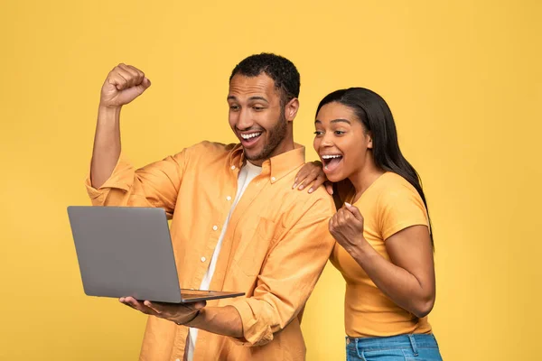 千年黑人夫妇做的是的手势 看笔记本电脑 庆祝成功或成就的黄色工作室背景 时髦的年轻夫妇对大减价或网上赢感到兴奋 — 图库照片