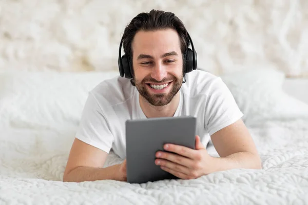 Feliz Barbudo Joven Acostado Cama Utilizando Nueva Tableta Digital Auriculares — Foto de Stock