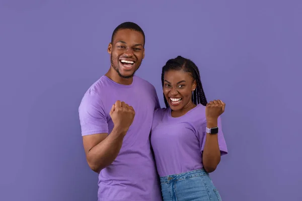 そうだ 喜びに満ちた若い黒人男性と女性の肖像画抱擁し レンズを向けた拳を振る 応援し カメラを見て 紫色の背景の壁の上に隔離された立ってポーズ興奮したカップル — ストック写真