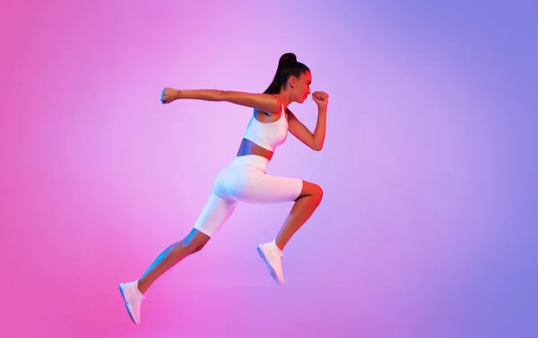 ピンクとブルーのネオンを背景に空中を走るスポーティレディ スタジオでフィットネストレーニング中に白いフィットネスウェアを身に着けて跳躍女性ランナー スポーツとアクティブライフ — ストック写真
