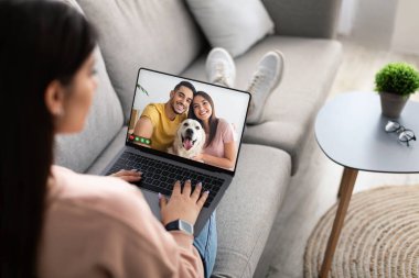 Genç bayanın gündelik koltukta oturup arkadaşlarıyla görüntülü görüşme yaparken, neşeli, çok ırklı bir çift ve köpekle modern dizüstü bilgisayar, online toplantı konsepti, kopyalama alanı...