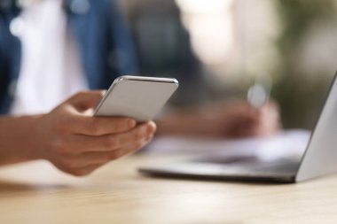 Genç Erkek 'in Laptop' la masamızda otururken modern akıllı telefonu kullanırken, cep telefonunu elinde tutarken, internetten alışveriş yaparken ya da göz gezdirirken, seçici odak noktasında çekilmiş fotoğrafı.