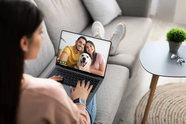 Genç bayanın gündelik koltukta oturup arkadaşlarıyla görüntülü görüşme yaparken, neşeli, çok ırklı bir çift ve köpekle modern dizüstü bilgisayar, online toplantı konsepti, kopyalama alanı...