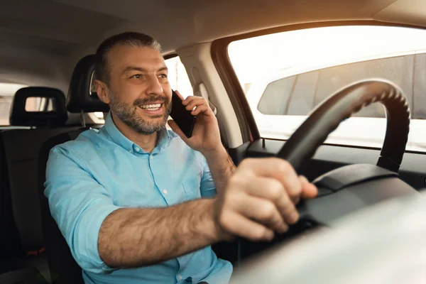 Portrait of cheerful male driver making cellular call having phone conversation while driving nice luxury car, busy positive middle aged guy talking on mobile phone, unsafe driving concept.