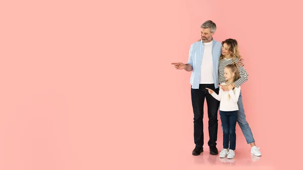 家庭奉献 快乐的中年父母和小女儿在空白空间的旁边投出带刺的指尖 拥抱着粉红工作室背景 看那里概念 — 图库照片