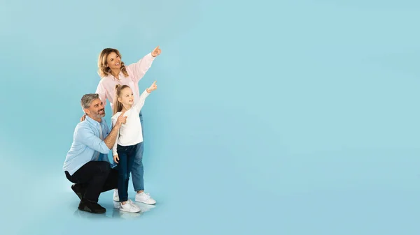 Szczęśliwa Rodzina Trzech Wskazujących Palcem Przestrzeń Kopiowania Stojąc Nad Niebieskim — Zdjęcie stockowe