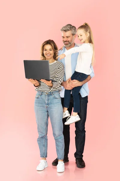 ラップトップブラウジングインターネットを使用して幸せな家族一緒に コンピュータで指を指す小さな娘ピンクのスタジオの背景の上に掲載ウェブサイトをお勧めします — ストック写真