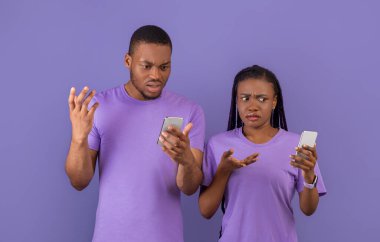 Garip Mesaj, Kötü Haber, İnternet Bağlantısı Sorunu. Kafası karışmış binlerce yıllık Afrika kökenli Amerikalı çift telefonlarına bakıyor ve omuzlarını silkiyor, mor menekşe arka planda tek başlarına duruyorlar.