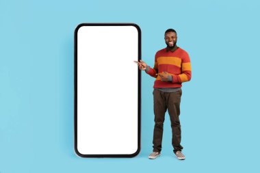 Şuna bak. Beyaz Ekranlı Büyük Boş Akıllı Telefonu Gösteren Siyah Adam Mobil Uygulama Tasarımı, Mavi Arkaplan, Mobil Fotokopi için Bedava Kopya Alanı Gösteren Gülümseyen Afrikalı Amerikalı Adam