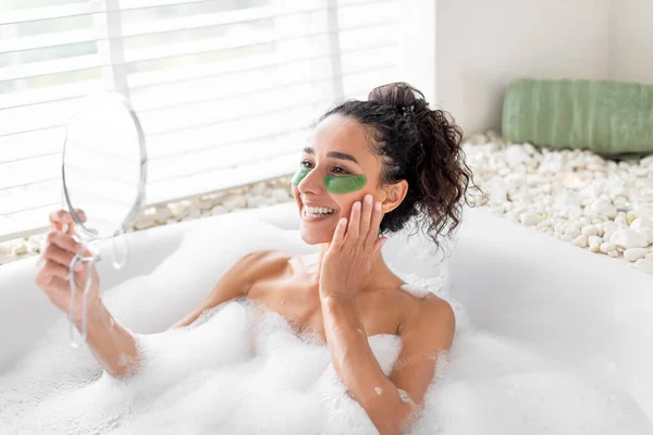 泡風呂に横たわっている間 鏡の前で目の下にパッチを適用するかなり若い女性は スペースをコピーします ホテルの浴槽で化粧品を使用して100万人の女性 美容日とホームスキンケア — ストック写真