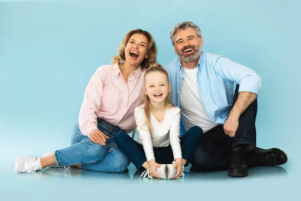 Joyful Family Laughing Together Sitting Looking At Camera Over Blue Studio Background. Parents And Daughter Having Fun Posing Expressing Positive Emotions. Joy And Happiness