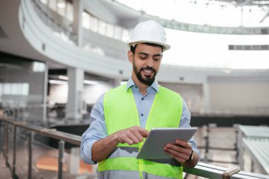 Sakallı, koruyucu giysili neşeli, genç Müslüman mühendis tablet yazarak fabrikanın içini kontrol ediyor. Başarılı iş için çevrimiçi teknoloji, fabrikada endüstri gelişimi