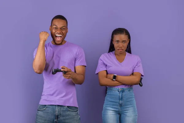 現代のオンラインゲームで勝利と損失の感情 幸せな興奮アフリカ系アメリカ人の男は 手にジョイスティックで拳を振る 成功を喜びます女性はカメラを見て動揺腕を折り畳む 紫の壁 — ストック写真