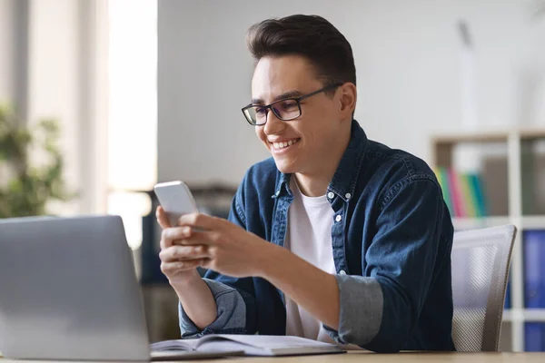 Sorrindo Jovem Empreendedor Masculino Usando Smartphone Enquanto Sentado Mesa Com — Fotografia de Stock
