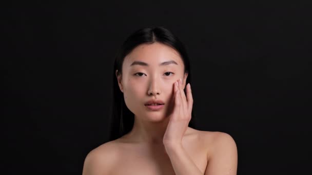 美容护理的秘密 年轻迷人的大韩民国女子裸露肩膀 在脸上涂上滋养乳霜 对着相机微笑 背景为黑色 动作缓慢的特写 — 图库视频影像