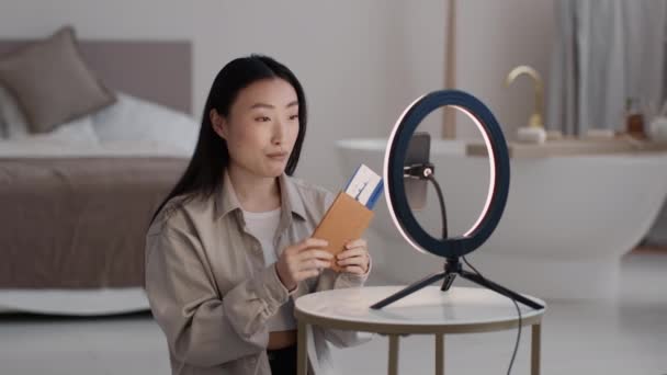 旅行博客 年轻漂亮的亚洲女人影响着记录她未来假期的视频 展示她的护照和智能手机的入场券 坐在家里 慢动作 — 图库视频影像