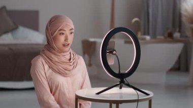 Canlı yayın. Genç, pozitif Müslüman Asyalı kadın blogcu akıllı telefondan video kaydediyor, internetten abonelerle sohbet ediyor, yavaş çekimde.