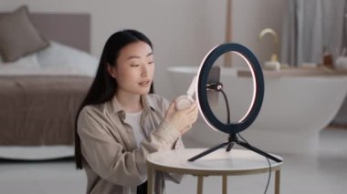 Çağdaş teknoloji konsepti. Milenyum Asyalı kadın blogcu yeni kulaklığı tanıtıyor, video incelemesi için evdeki video bloğunda modern cihazın reklamını yapıyor, yavaş çekim.