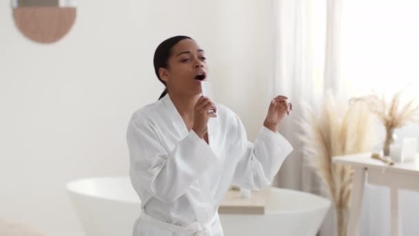 バスローブの若い黒人女性のマイクのようなヘアブラシには 自宅で朝のシャワーの後に踊り スローモーションを歌う 音楽の概念 — ストック動画