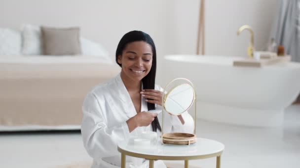 年轻漂亮的非洲裔美国女士穿着浴衣 梳着她那笔直而健康的头发 看着家里的镜子 自由自在 — 图库视频影像