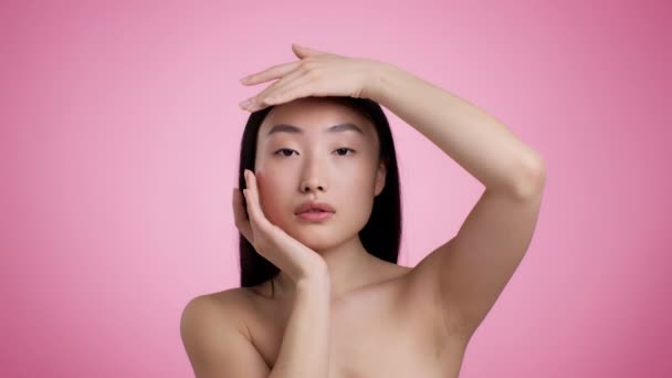 Facebuilding Concept 年轻迷人的亚裔女士摸着脸 在粉色背景下看着相机 慢动作的工作室肖像 — 图库视频影像