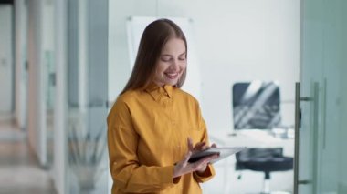 Genç mutlu bayan çalışan web sörfü dijital tablet ve gülümseme, çevrimiçi araştırma, ofis koridorunda durmak, yavaş çekim, serbest alan
