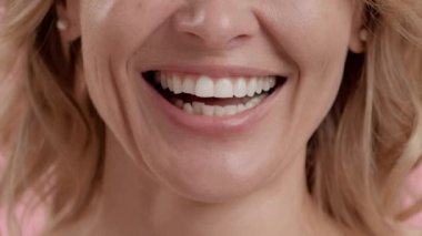 Diş sağlığı ve stomatoloji konsepti. Kameraya gülümseyen, diş hizalama prosedüründen sonra gülümseyen, yavaş çekim yapan, tanınmayacak kadar olgun, beyaz bir kadının yakın plan çekimi.